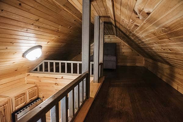 modular log cabin with wood ceiling and walls in loft space with dark railings