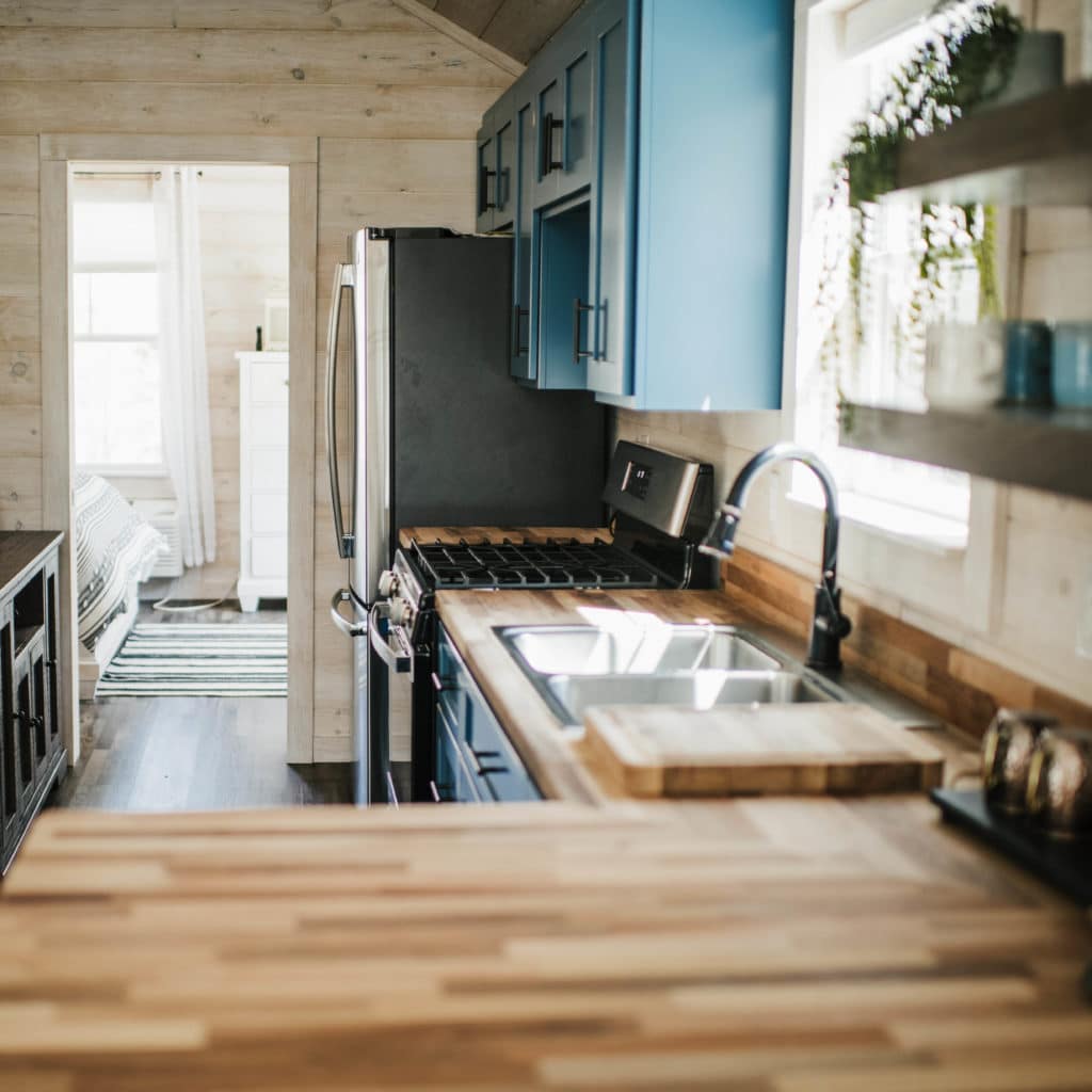 cottage style kitchen with blue accent cabinets and wood counters in modular tiny home