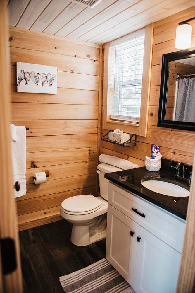 wooden interior bathroom with white cabinet and dark countertop in modular tiny log cabin